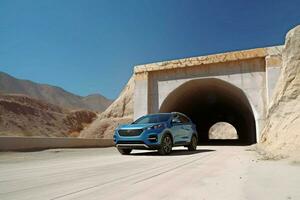 a blue kia sportage is parked under a bridge in the photo