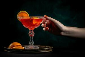 a hand holding a red cocktail glass with a slice photo