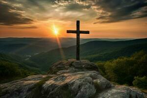 cross on a mountain with the sun setting behind it photo