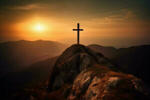 cross on a mountain with the sun setting behind it photo