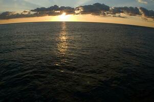 un barco es navegación a través de el Oceano a puesta de sol foto