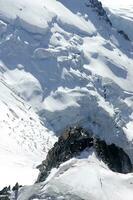 dos personas son excursionismo arriba un montaña con nieve cubierto montañas foto