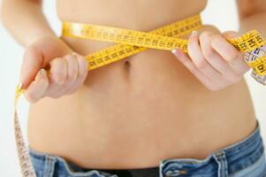 a woman is measuring her waist with a tape measure photo