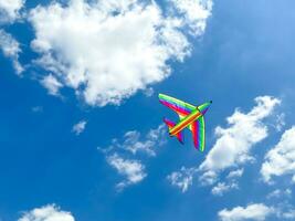 Multicolored kite flies in the blue sky on a sunny day. Empty space for an inscription. Multicolored kite in the form of an airplane. photo