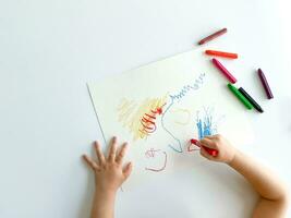 small child draws with pastel crayons on white table. photo