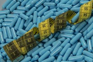 Blue weight loss pills and measuring tape symbolizing slimming photo