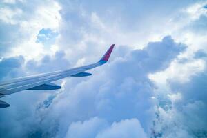 Clear blue sky with fluffy ornamental cumulus clouds, panoramic view from an airplane, wing close-up. Dreamlike cloudscape. Travel, tourism, vacations, turbulence. photo