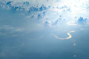 Aerial view from airplane window of white puffy clouds on bright sunny day ang glowing river. photo