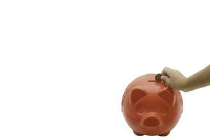 child hand putting coin into piggy bank from the top view isolated on white background, saving concept. Copy space for your text photo