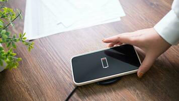 Charging mobile phone battery with wireless charging device in the table. Smartphone charging on a charging pad. Mobile phone near wireless charger Modern lifestyle technology concept. photo