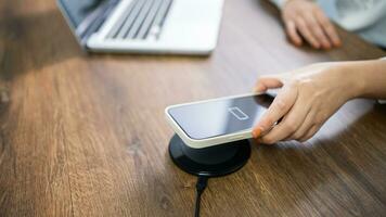 Charging mobile phone battery with wireless charging device in the table. Smartphone charging on a charging pad. Mobile phone near wireless charger Modern lifestyle technology concept. photo