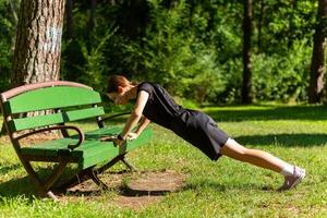 hermosa joven deportivo mujer en negro camiseta, negro pantalones cortos y rosado entrenadores calentamiento arriba hacer ejercicio triceps y cofre foto