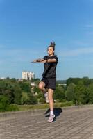 Young, fit and sporty girl in black clothes stretching after the workout in the urban city park. photo