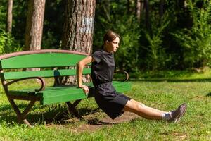 hermosa joven deportivo mujer en negro camiseta, negro pantalones cortos y rosado entrenadores calentamiento arriba hacer ejercicio triceps foto