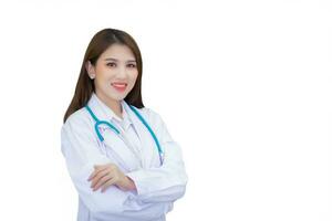 profesional joven asiático mujer médico vistiendo blanco túnica y estetoscopio en pie con brazos cruzado contento y sonrisa a examen habitación en hospital mientras aislado en blanco antecedentes. foto