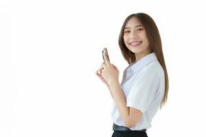 Portrait of cute young Asian Thai girl student in uniform is smiling happily while using smartphone for finding educational information at university while isolated on white background. photo