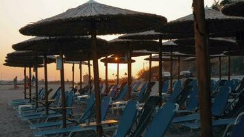 Beach with straw umbrellas and deck chairs at sunset, Greece video