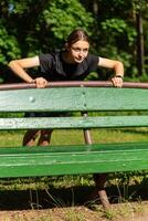 hermosa joven deportivo mujer en negro camiseta, negro pantalones cortos y rosado entrenadores calentamiento arriba hacer ejercicio triceps y cofre foto