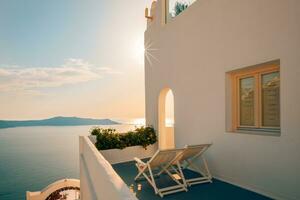 arquitectura blanca en la isla de santorini, grecia. restaurante al aire libre bajo un fantástico paisaje de puesta de sol, sillas para pareja. vista romántica de la puesta de sol, cielo naranja y nubes. vacaciones de verano, viajes de luna de miel foto