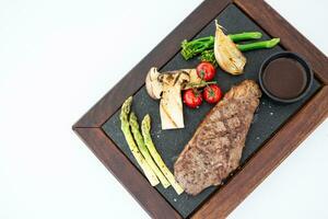 BBQ Steak in luxury restaurant on white counter top view. Barbecue grilled beef steak meat with fresh tomatoes, asparagus, mushroom slices. Healthy food. Barbecue steak dinner, gourmet cuisine photo