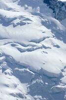 dos personas son excursionismo arriba un montaña con nieve cubierto montañas foto