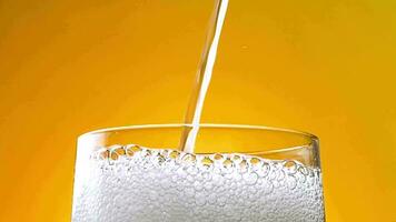 scrosciante carbonato acqua in un' bicchiere. giallo arancia sfondo, lento movimento video. bolle nel il bicchiere. video