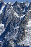 two people are hiking up a mountain with snow covered mountains photo