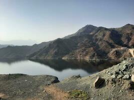 A beautiful daytime view of  Wadi Qanuna Dam in Al Bahah, Saudi Arabia. The water of the dam and the surrounding hills are presenting a beautiful scene in the sunlight. photo