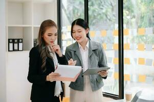 Two Asian businesswoman and man discuss investment project working and planning strategy with tablet laptop computer in office. photo