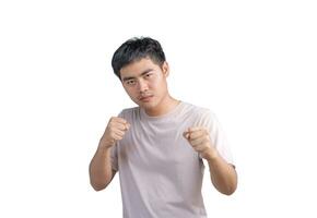 joven hermoso hombre vistiendo casual camiseta terminado blanco antecedentes. puñetazos puño a luchar, agresivo y enojado ataque, amenaza y violencia, mirando adelante en boxeo puños y Listo a ataque. foto