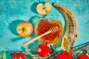 rosh hashaná - judío nuevo año fiesta concepto. cuenco en el forma de un manzana con Miel, manzanas, granadas, shofar en un azul antecedentes foto