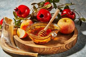 rosh hashaná - judío nuevo año fiesta concepto. cuenco en el forma de un manzana con Miel, manzanas, granadas, shofar en un azul antecedentes foto
