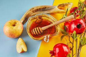 Rosh hashanah - jewish new year holiday concept. Bowl in the form of an apple with honey, apples, pomegranates, shofar on yellow-blue background photo