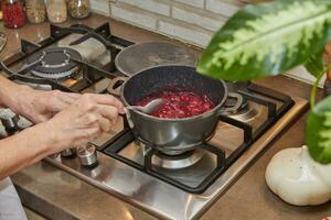 Chef cooks cherries in saucepan on a gas stove photo