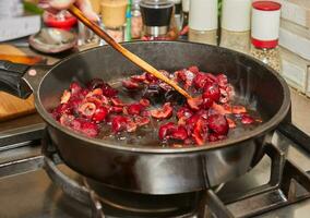 Chef fries fresh cherries in caramel syrup in frying pan on gas stove photo