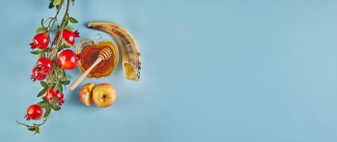 Rosh hashanah banner - jewish new year holiday concept. Bowl in the shape of an apple with honey, apples, pomegranates, shofar on blue background. photo