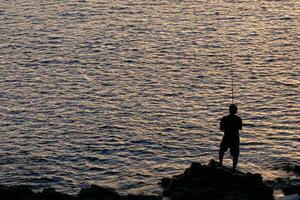 hombre retroiluminado con un pescar varilla en el mar foto