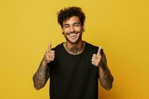 sonriente alegre joven Hispano hombre con tatuajes cruce dedos siendo optimista en amarillo antecedentes foto