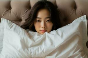 Unsettled Asian woman concealing face with pillow in living room photo