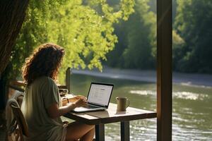 Female freelancer sitting and working on a laptop in a cafe by the river photo