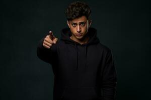 Young Hindu man in black hoodie happily points to blank space for your ad photo