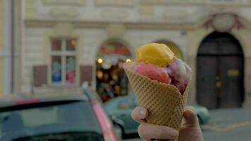 Slow motion close up view of walking woman eats ice cream balls against unfocused cityscape on the background, Prague, Czech Republic video