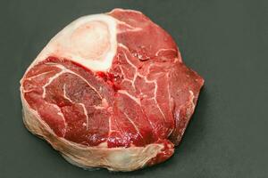 Fresh piece of meat large beef steak on the bone ossobuco with a sprig of rosemary on a black background photo