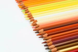 Multi-colored pencils lie on a white table, the red range of colors photo