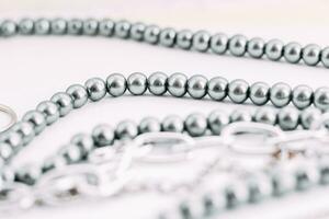 A necklace of gray beads with chain decorations on a white aesthetic background. photo