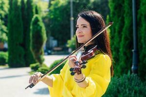 Woman artist with dark hair in a dress plays a wooden concert electric violin photo