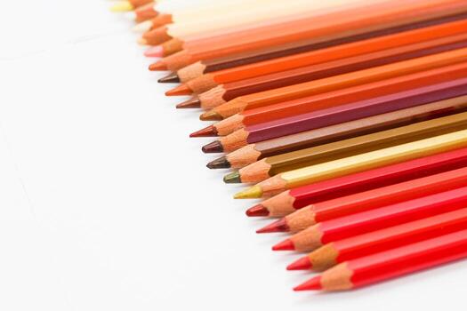 Multi-colored pencils lie on a white table, the red range of colors photo