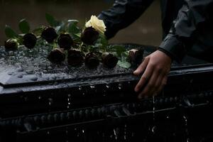 de cerca de un funeral ataúd a un cementerio con flores en el lluvia, mano en el tumba en el lluvia con oscuro antecedentes y Rosa ai generado foto