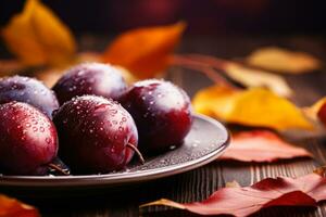 Closeup of fresh plums with water drops on plate on beige table with brown fall leaves in background photo