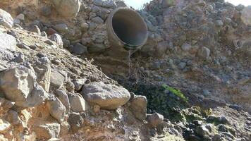 Waste water flows out of a sewage pipe into a sandy hole. video